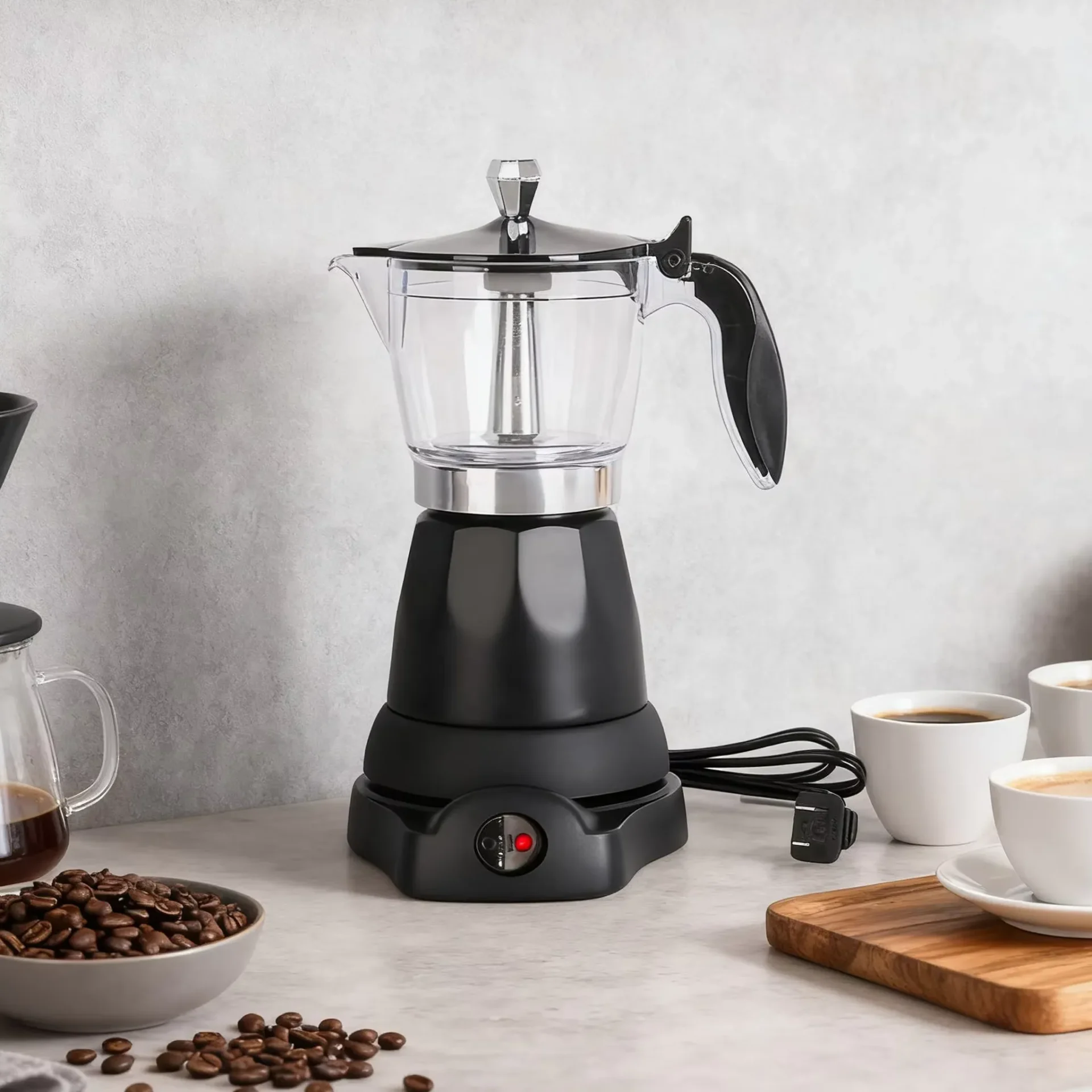 Cafetera moka eléctrica de color negro y jarra transparente sobre una encimera de mármol, rodeada de granos de café, tazas blancas con café y una tabla de madera.