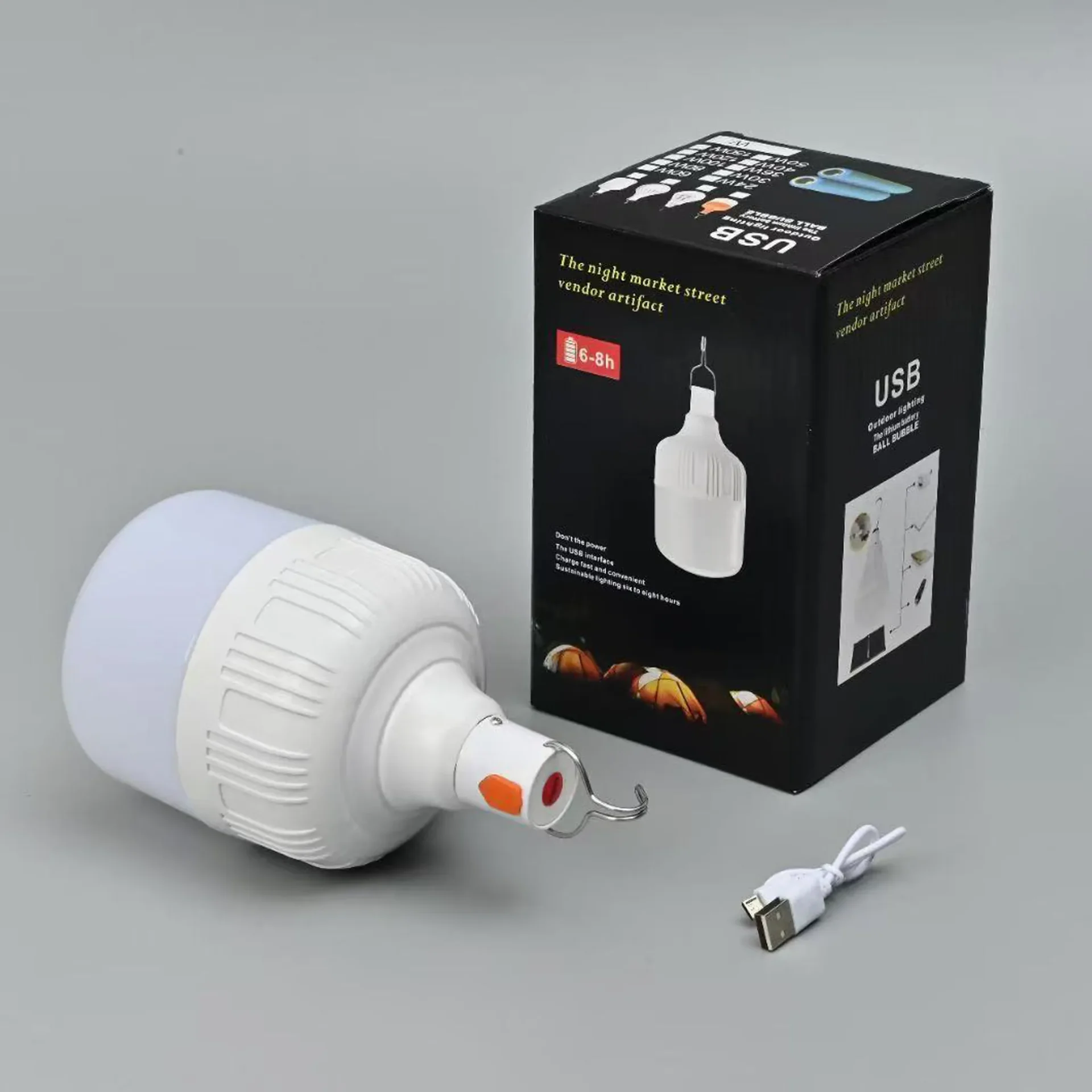 Kit de bombilla LED portátil blanca con su caja de empaque negra y cable de carga USB blanco; la bombilla incluye un gancho para colgar y un botón naranja, sobre fondo gris.